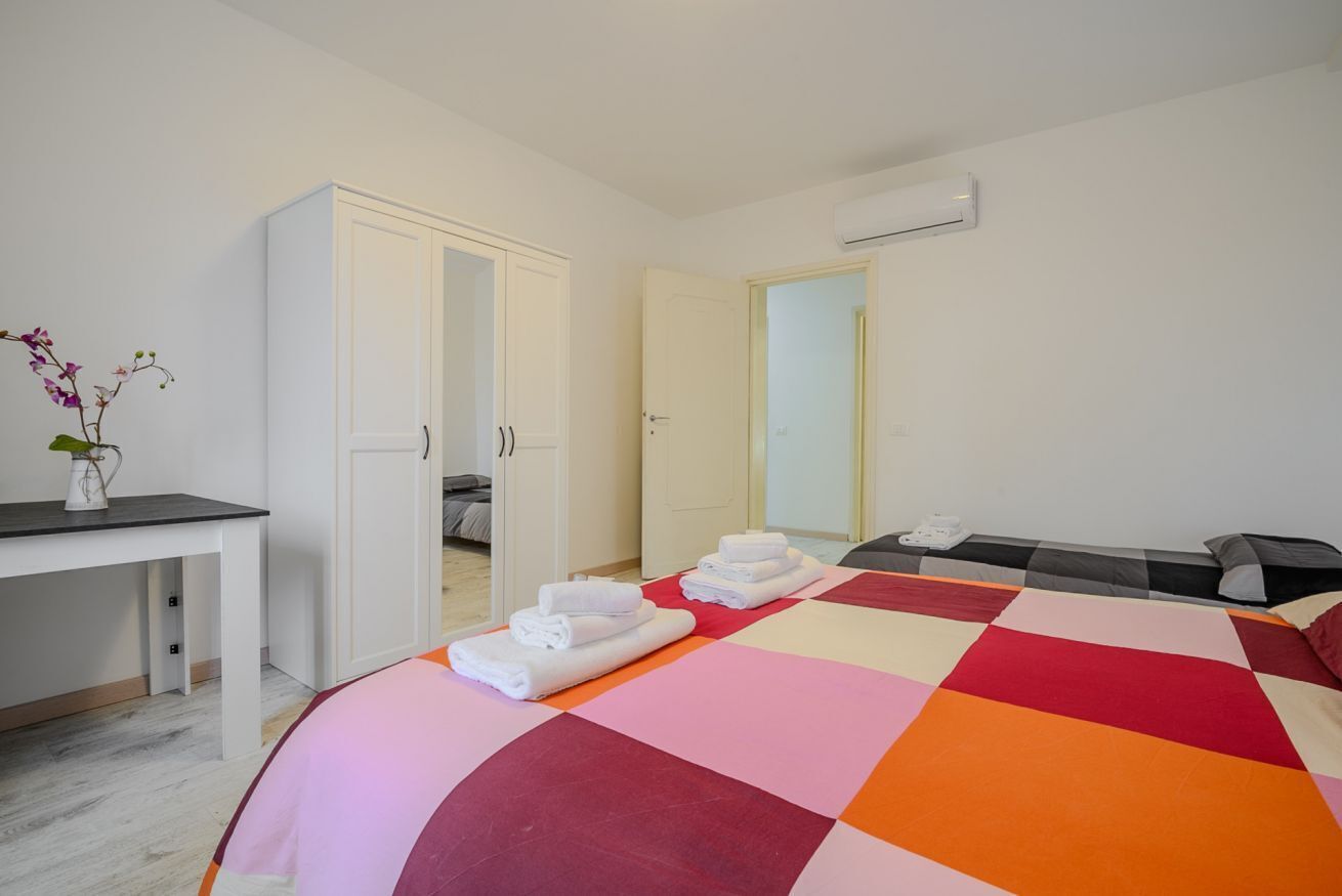 A hotel room with a bed, a desk, a wardrobe, and an air conditioning unit.