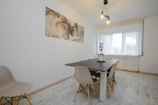 A dining area with a dark wooden table, four chairs, a single flower vase, a large painting of lions, and a window with sheer curtains. - Ponte Milvio apartment Flaminio (Roma)