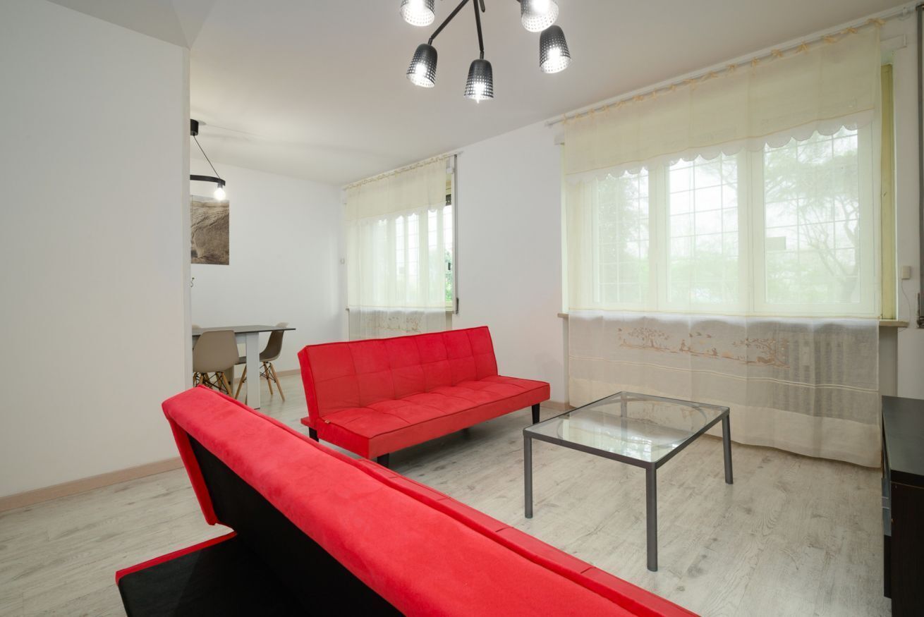 A living room with a red sofa, a glass coffee table, and a ceiling light fixture.