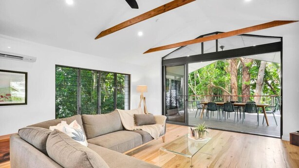 Una sala moderna con un sofá seccional, una mesa de centro de vidrio y vistas a una terraza exterior con sillas.