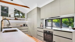 Una cocina moderna con una isla grande, electrodomésticos de acero inoxidable y un ventanal con vistas a la vegetación.