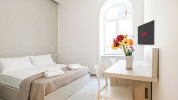 Een moderne hotelkamer met een bed, een bureau met stoel, een televisie en een raam met bloemen.