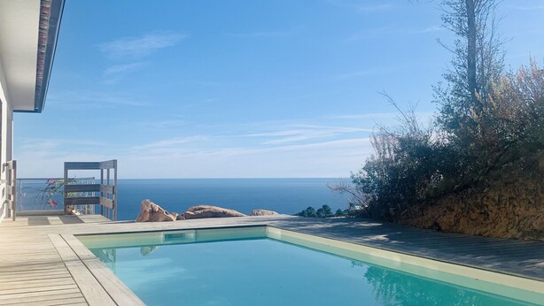 A swimming pool with a wooden deck, a view of the ocean, and a rocky landscape. - Appartement Spacieux, vue Splendide sur la mer Avec Piscine Privée (Sari-Solenzara)