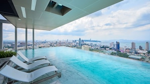 An infinity pool with a city view, lounge chairs, and a clear sky. - Once condo - Pattaya central location  (Pattaya)