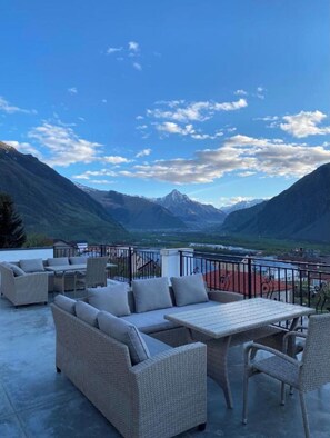 An outdoor seating area with wicker furniture and a table, overlooking a mountainous landscape with a clear sky. - MOOD HOTEL KAZBEGI (Kazbegi)