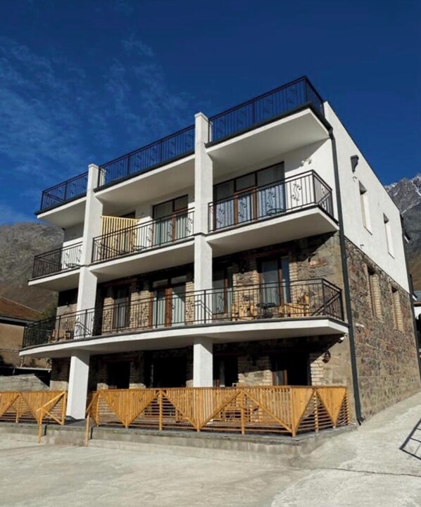 A multi-story building with balconies, a stone facade, and a mountainous backdrop. - MOOD HOTEL KAZBEGI (Kazbegi)
