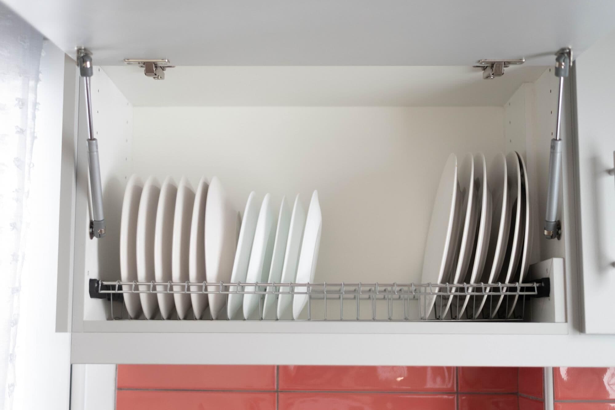 A kitchen with a dish rack holding white plates and a red tiled backsplash.