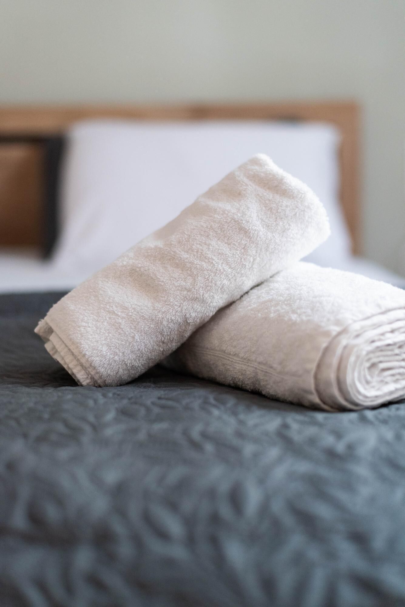 Une serviette beige, soigneusement pliée, est posée sur un couvre-lit foncé à texture marquée.