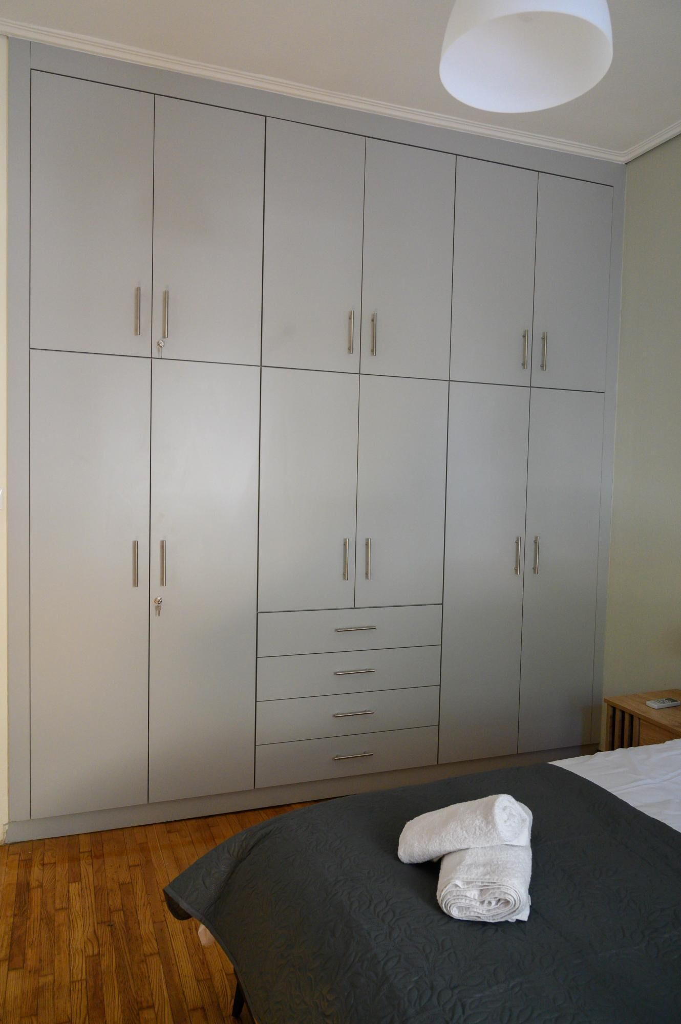 A bedroom with a large wardrobe, a bed with a grey bedspread, and a wooden floor.