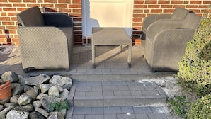 Tiilestä rakennettu rakennus, jossa on patioalue, jossa on rottinkihuonekaluja ja kivestä tehty polku.