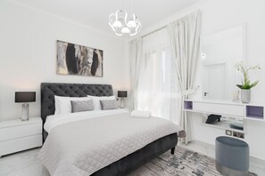 Relax in this serene bedroom with a tufted headboard bed, chandelier, and TV.