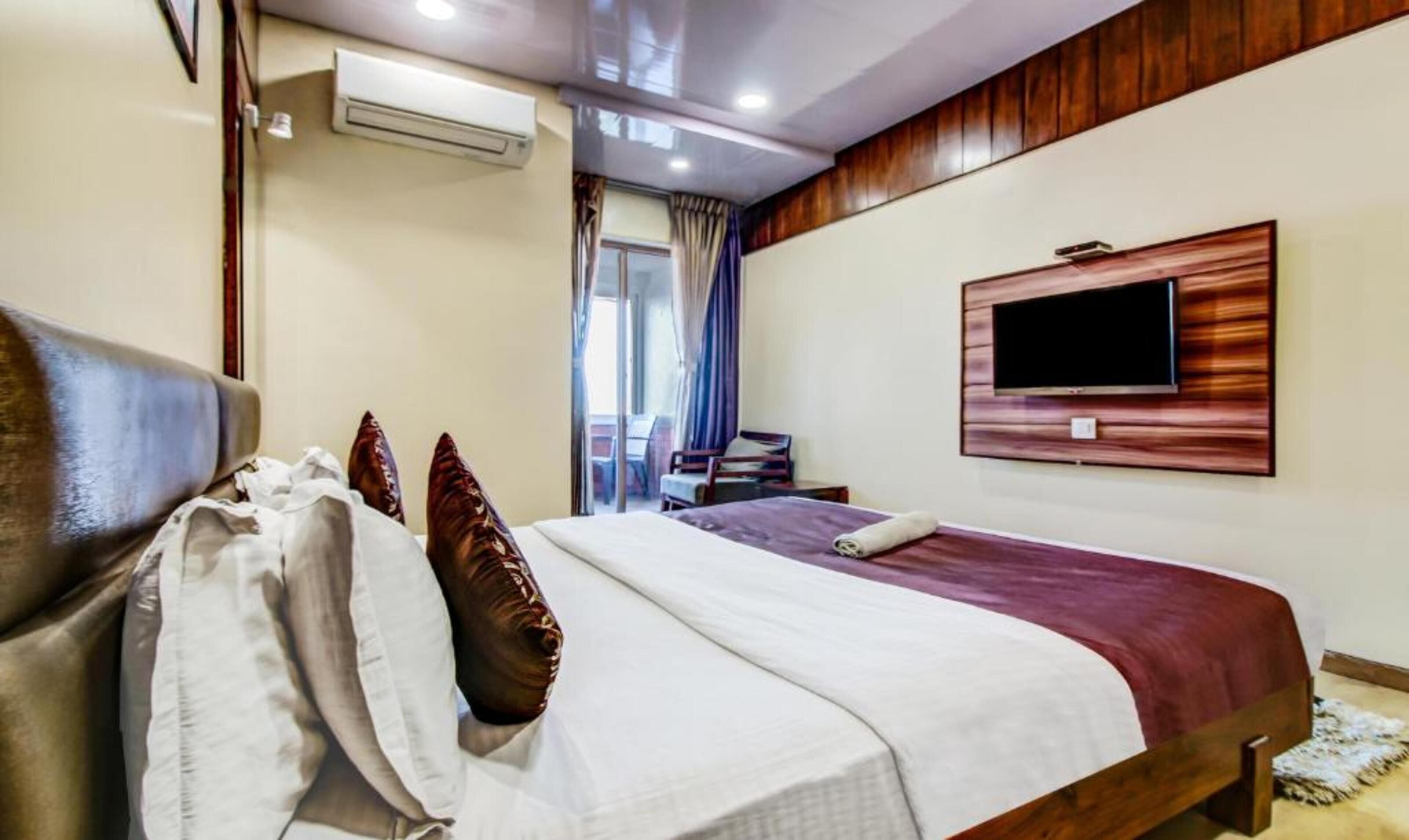 A hotel room with a bed, a TV mounted on the wall, and an air conditioning unit.