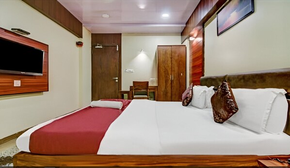 A hotel room with a large bed, wooden headboard, a TV mounted on the wall, and a wardrobe. - Hotel Shree Daan (Vapi)