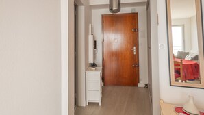 A narrow hallway with a wooden door at the end, a small white cabinet, and a mirror on the wall. - 1-bedroom apartment with balcony, beachfront location (Les Sables-d'Olonne)