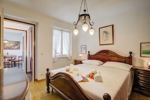 A hotel room with a wooden bed, a chandelier, a dining area, and artwork on the walls.