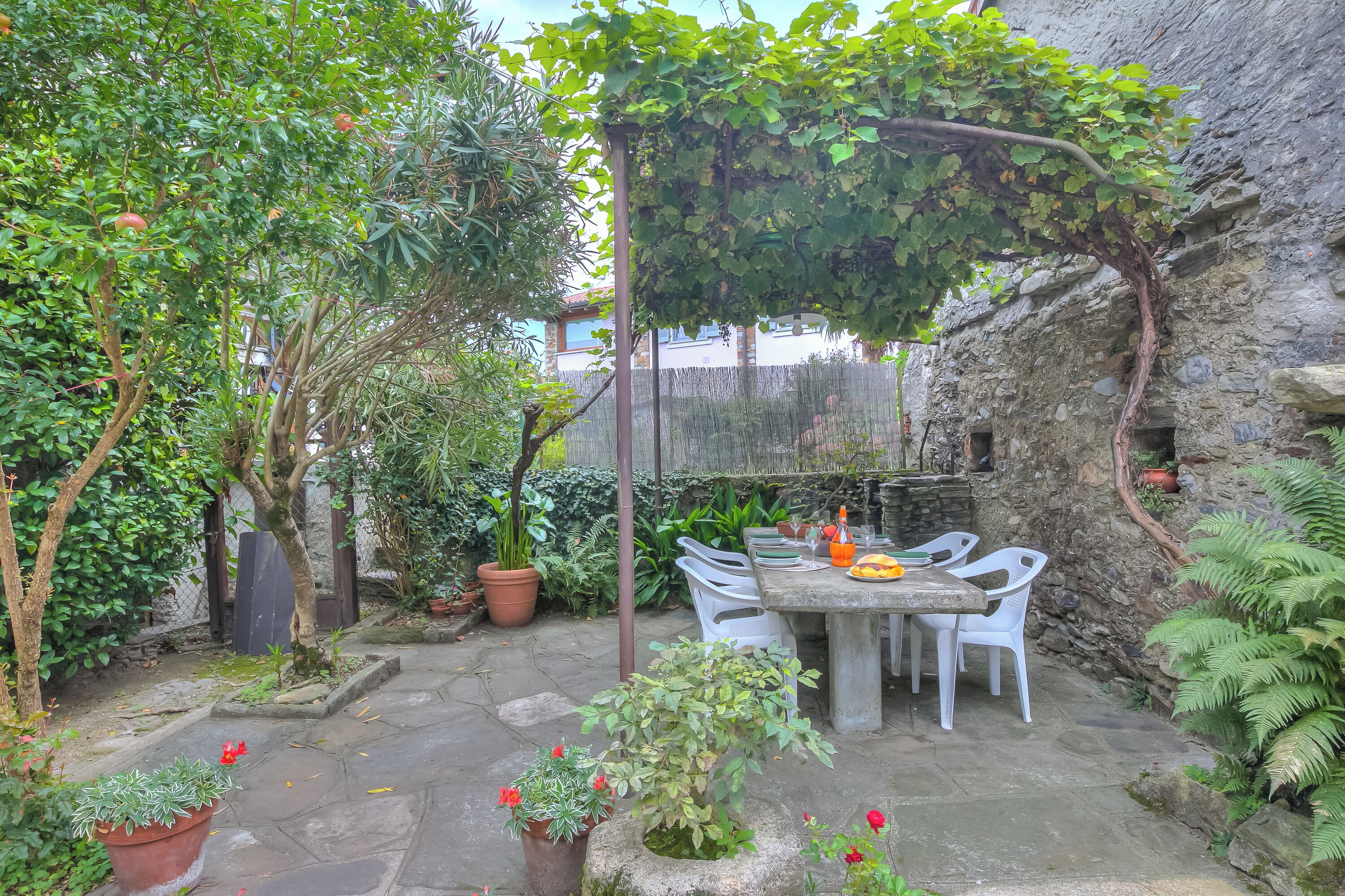 A patio with a table and chairs, surrounded by potted plants and a stone wall.