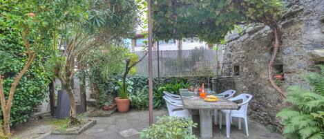 A patio with a table and chairs, surrounded by potted plants and a stone wall.