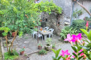 A stone patio with a table and chairs, surrounded by potted plants and a stone wall. - Il Cortiletto di Marina Pet Friendly (Brovello-Carpugnino)