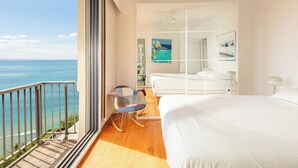 Un balcon avec vue sur l’océan, un lit, une chaise et un ventilateur de plafond.