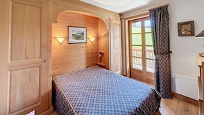 Une pièce avec un lit, des murs en bois, un tableau accroché au mur et une porte donnant sur l’extérieur.