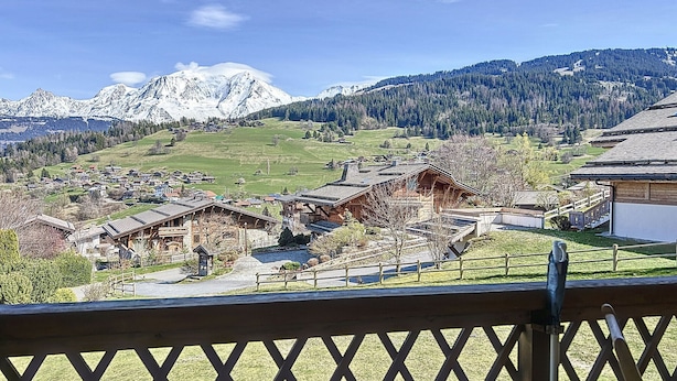 Un village de montagne aux maisons traditionnelles en bois, avec un ciel dégagé et des sommets enneigés en toile de fond.