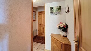 A hallway with a wooden door, a radiator, a wall-mounted picture, and a vase with flowers. - Apartment with garage near ski bus in Combloux (Combloux)