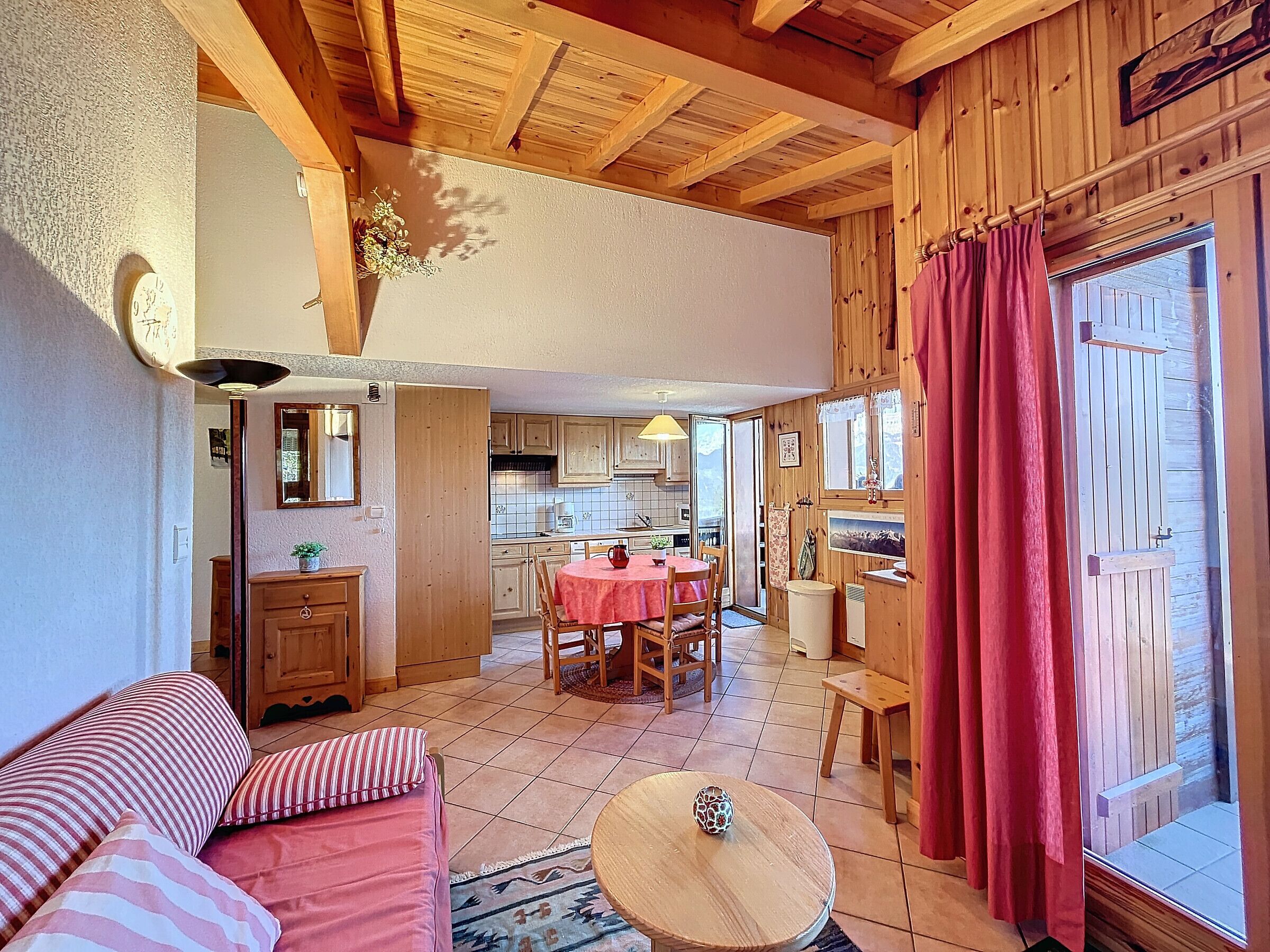 A cozy room with a wooden ceiling, a dining area with a table and chairs, and a kitchen visible through an open door.