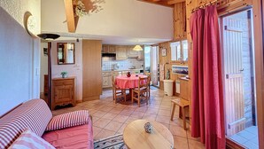 A cozy room with a wooden ceiling, a dining area with a table and chairs, and a kitchen visible through an open door. - Apartment with garage near ski bus in Combloux (Combloux)