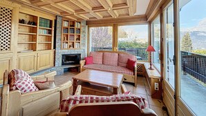 Un salon chaleureux avec une cheminée, des étagères en bois et une grande fenêtre donnant sur l’extérieur.