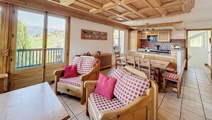 Un intérieur de chalet chaleureux, avec des meubles en bois, un coin cuisine et de grandes fenêtres offrant une vue panoramique.