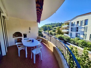 A balcony with a round table and chairs, a small brick fireplace, and a view of a residential area with buildings and parked cars. - 3-Room Apartment Near Beach & Shops with Terrace, Parking - Sleeps 5, Cavalaire-sur-Mer (Cavalaire-sur-Mer)