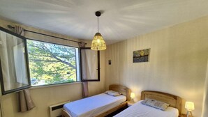 Una stanza con due letti singoli, una finestra con tende, un lampadario e un piccolo quadro appeso al muro.