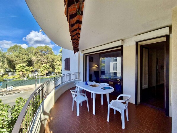A balcony with a table and chairs, a hanging plant, and a view of trees and buildings. - 3-Room Apartment Near Beach & Shops with Terrace, Parking - Sleeps 5, Cavalaire-sur-Mer (Cavalaire-sur-Mer)