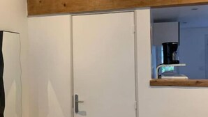 A room with a white wardrobe, a wooden beam above the door, and a small mirror on the wall.