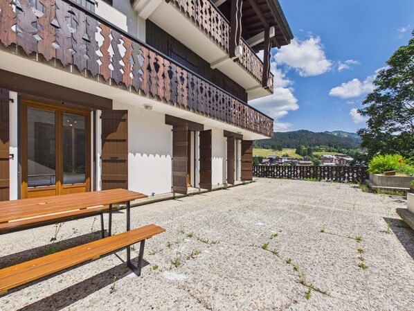 Un edificio con balcón de madera, patio de grava y vista a un paisaje montañoso.
