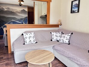 En moderne stue med en grå sofa, to puder med mønster, et rundt træbord og et stort spejl over sofaen.