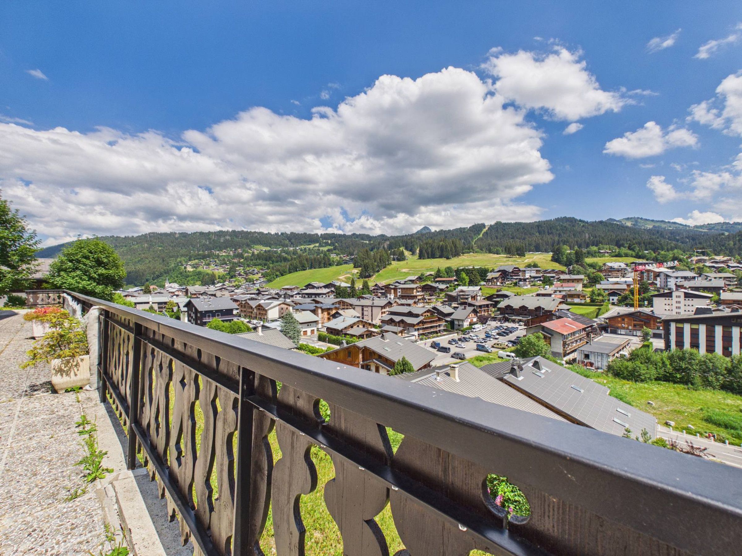 A town with traditional wooden buildings, a bridge with decorative railings, and a mountainous backdrop.