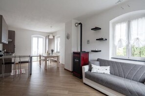 Un soggiorno moderno con un divano grigio, un'area pranzo con tavolo e sedie, una cucina con un elettrodomestico rosso e un'ampia finestra con tende.