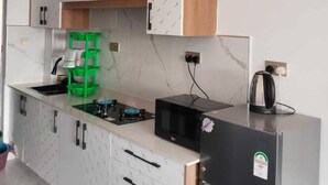A compact kitchen with white cabinets, a black refrigerator, a green drying rack, and a kettle on the counter. - Comfort Homestay Kilimani (Nairobi)