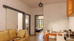A cozy living room with a sofa, a dining table with a pot and a bottle, and a kitchen area with a stove. - Kings Hotel by Estia (Hersonissos)