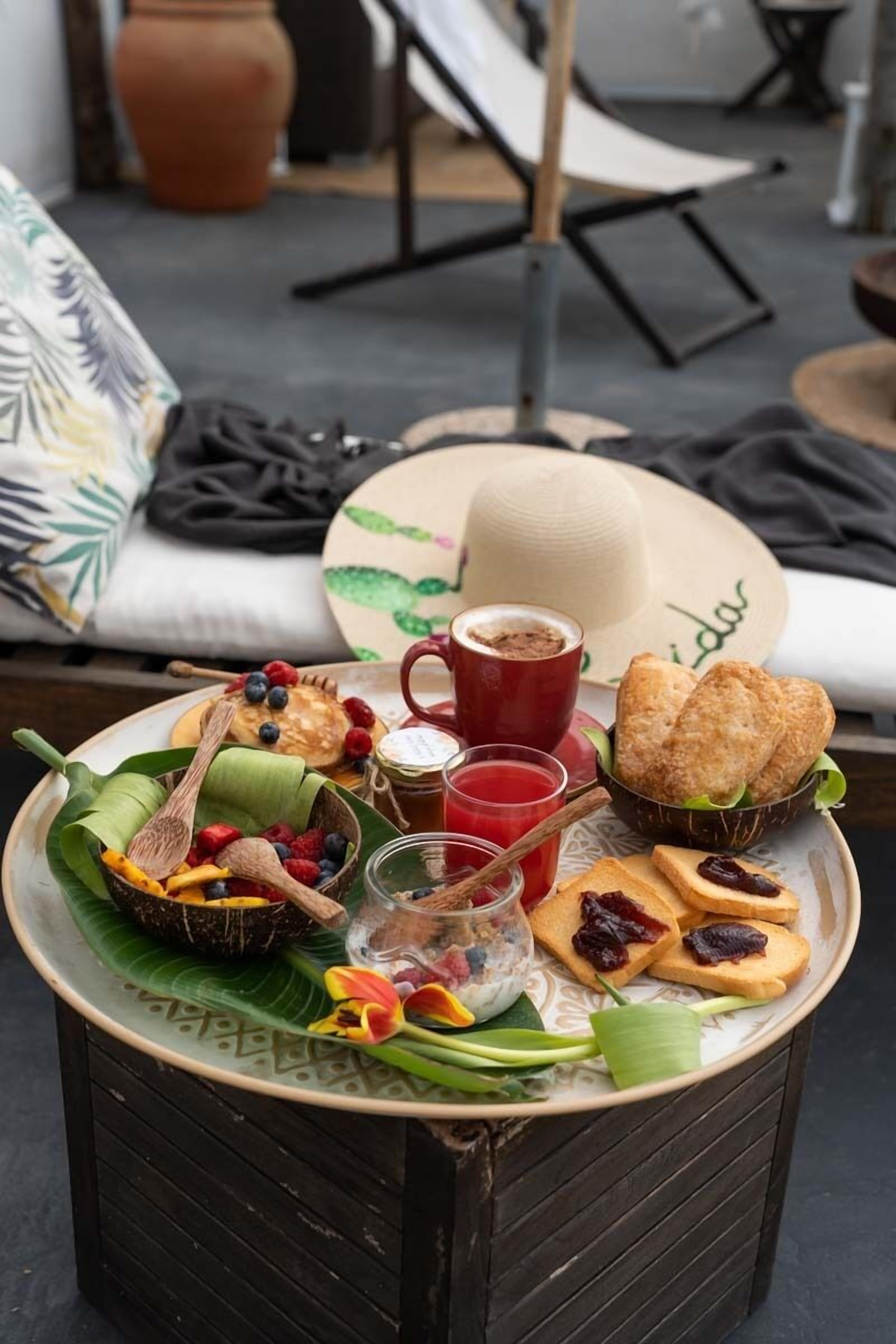 A breakfast tray with pancakes, berries, a cup of coffee, and pastries on a wooden table.