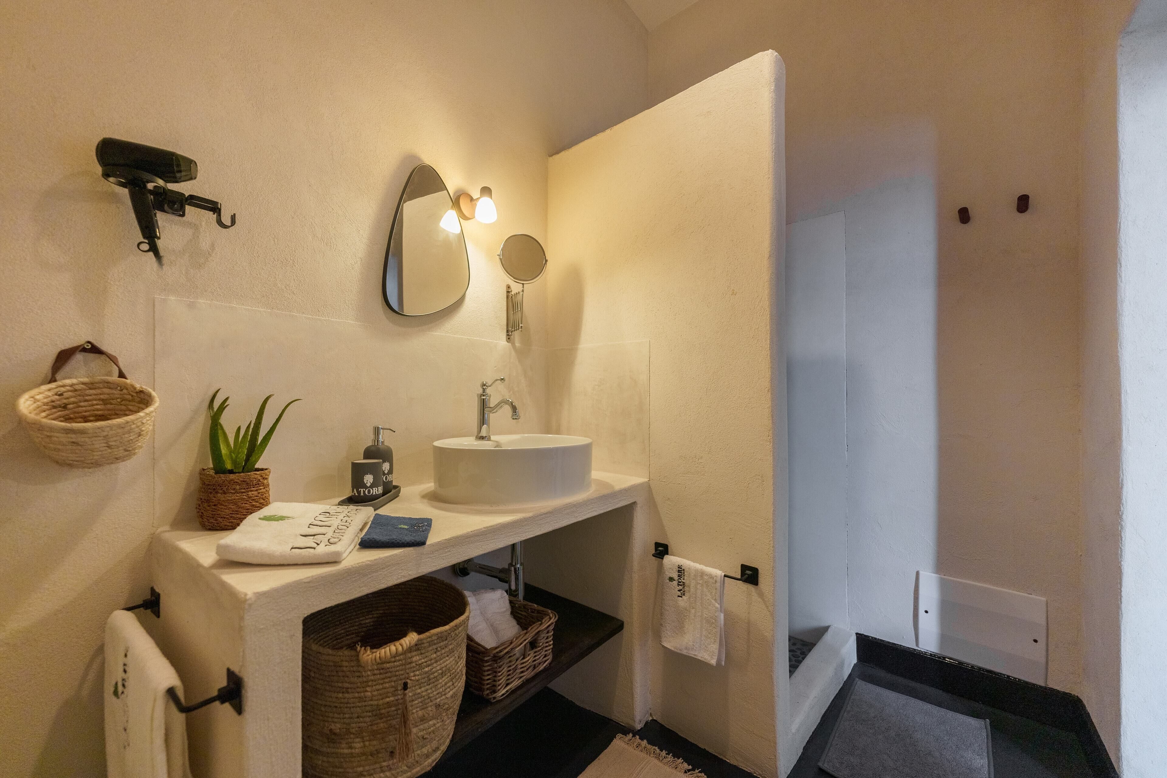 A bathroom with a white sink, a mirror, a towel rack, a basket, and a potted plant.