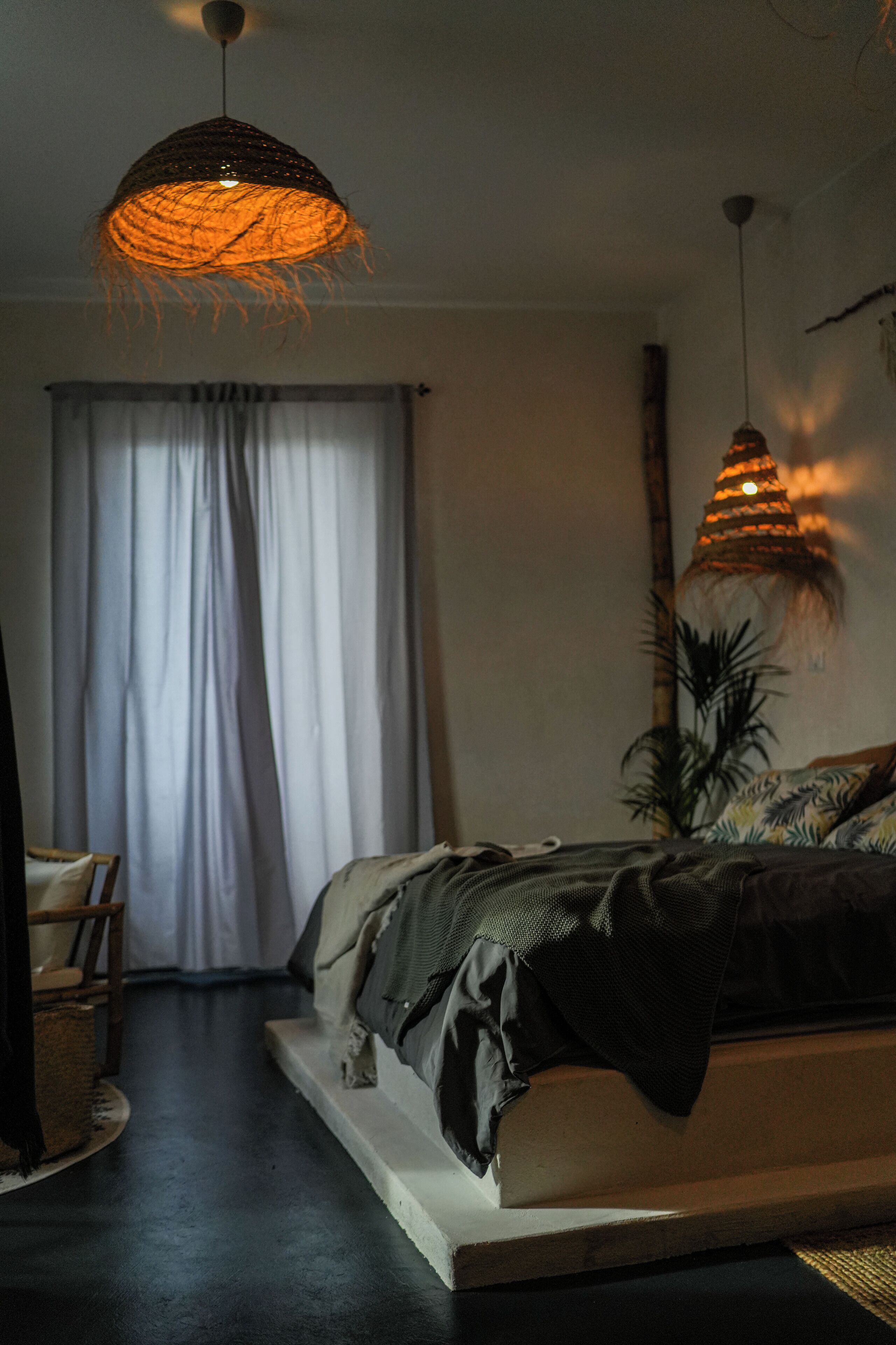 A bedroom with a bed, a hanging light fixture, a plant, and a window with curtains.