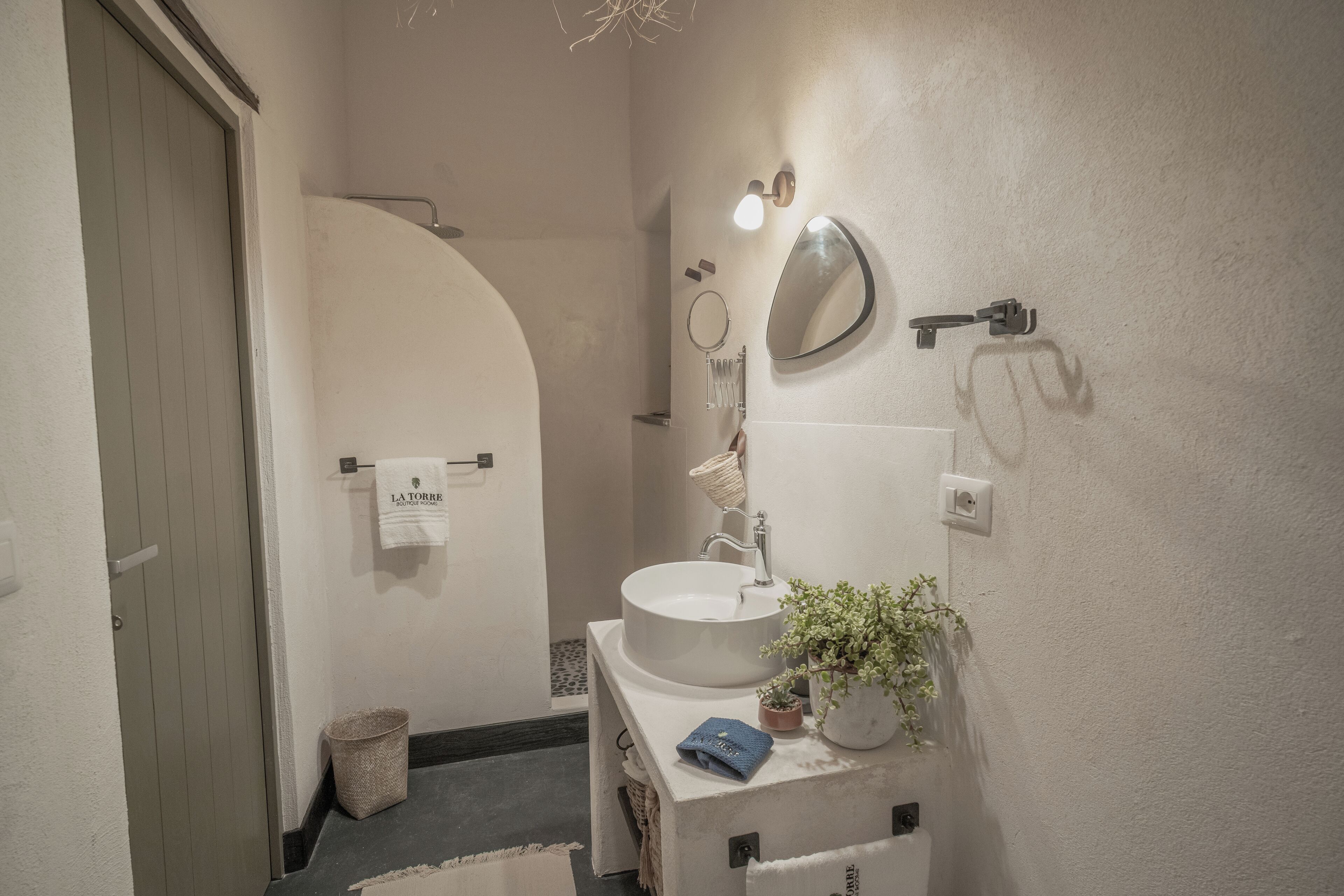 Une salle de bain avec un lavabo blanc, un miroir, un porte-serviettes, une plante en pot et une serviette accrochée au mur.