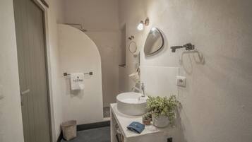 Une salle de bain avec un lavabo blanc, un miroir, un porte-serviettes, une plante en pot et une serviette accrochée au mur.