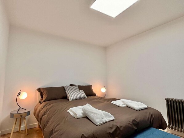 Ein Schlafzimmer mit einem großen Bett, zwei Nachttischlampen, einer Heizung und einem Oberlicht.