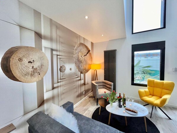 Un salon moderne avec un canapé, un fauteuil jaune, une table basse ronde et une grande fenêtre donnant sur un beau paysage.