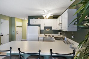 Cozinha com armários brancos, fogão, pia e ventilador de teto.