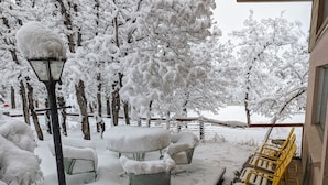 A snow-covered outdoor seating area with metal chairs and tables, surrounded by snow-laden trees.