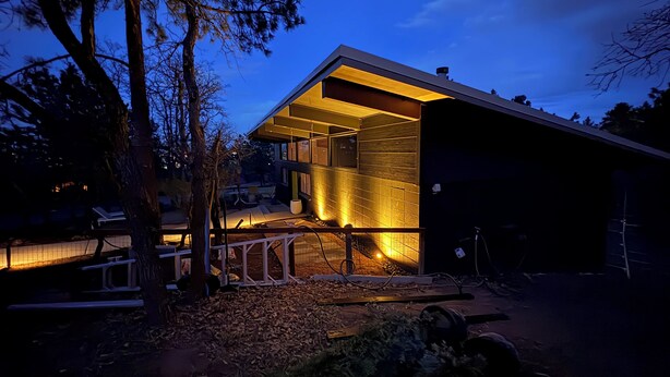 A modern house with a large open porch and a covered outdoor area, surrounded by trees.
